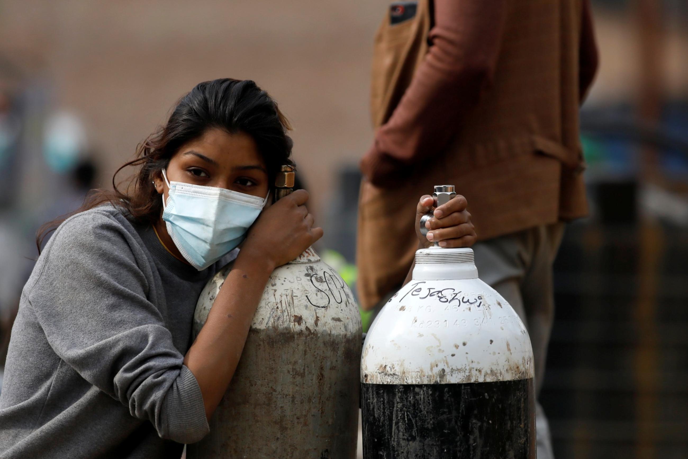 a young woman wearing a light blue surgical face mask rests her head on an empty oxygen tank