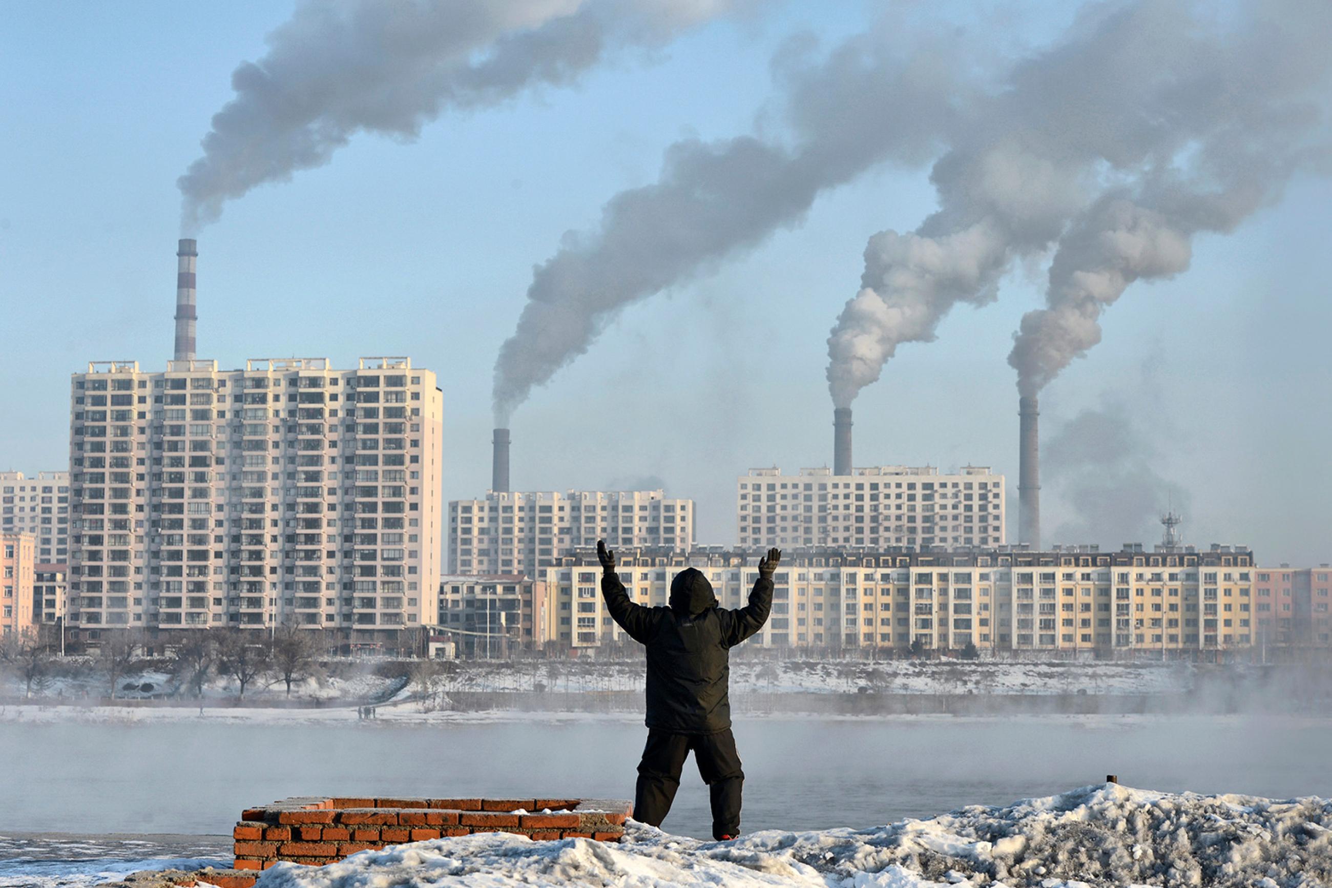 Factories emit smoke in Jilin province, China, across the Songhua River from where an elderly man exercises on the morning of Feb 24, 2013, after Chinese authorities announced plans to curb pollution. The photo shows the man in the foreground, back to the camera, with buildings on the other side of the river pouring out smoke. REUTERS/Stringer