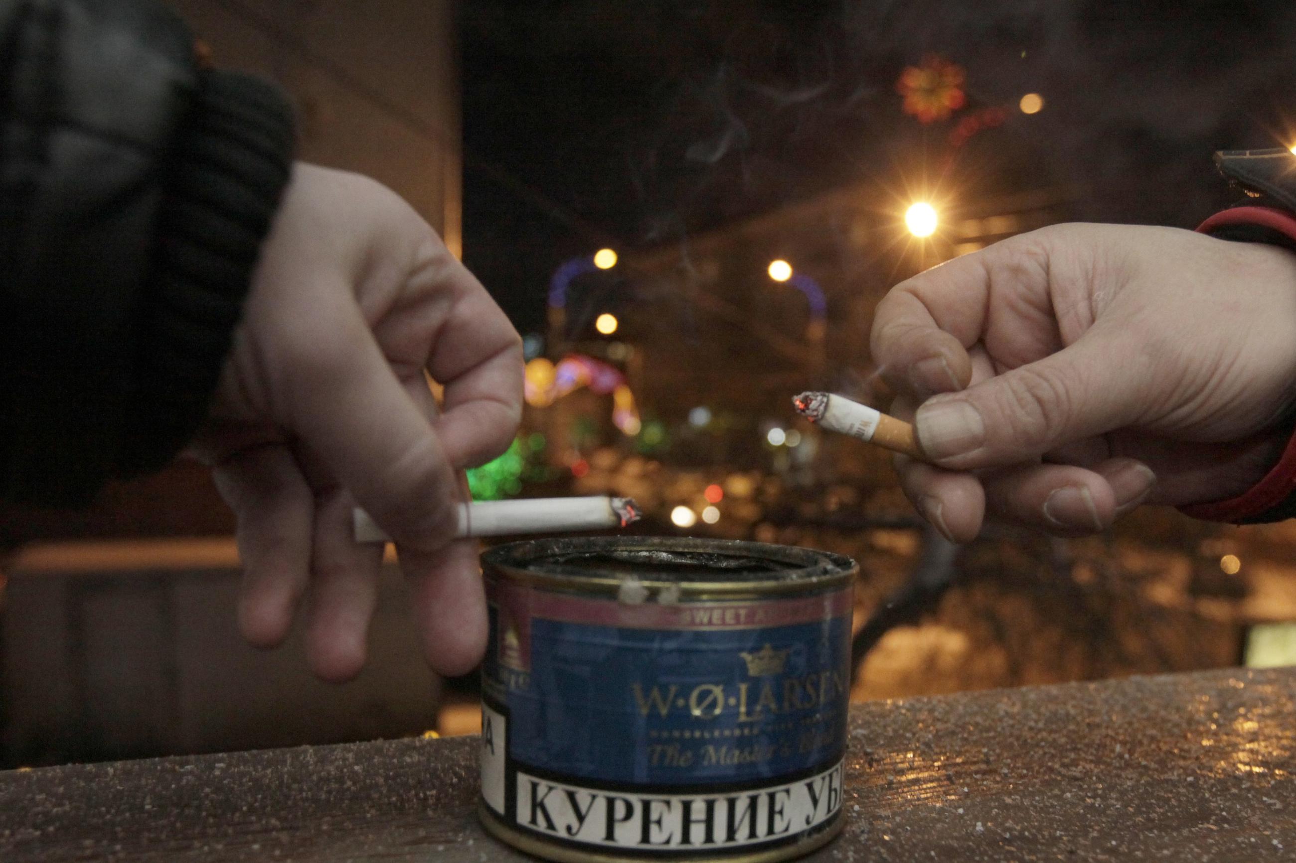 Men tap ash from their cigarettes while smoking on the balcony of an office building.