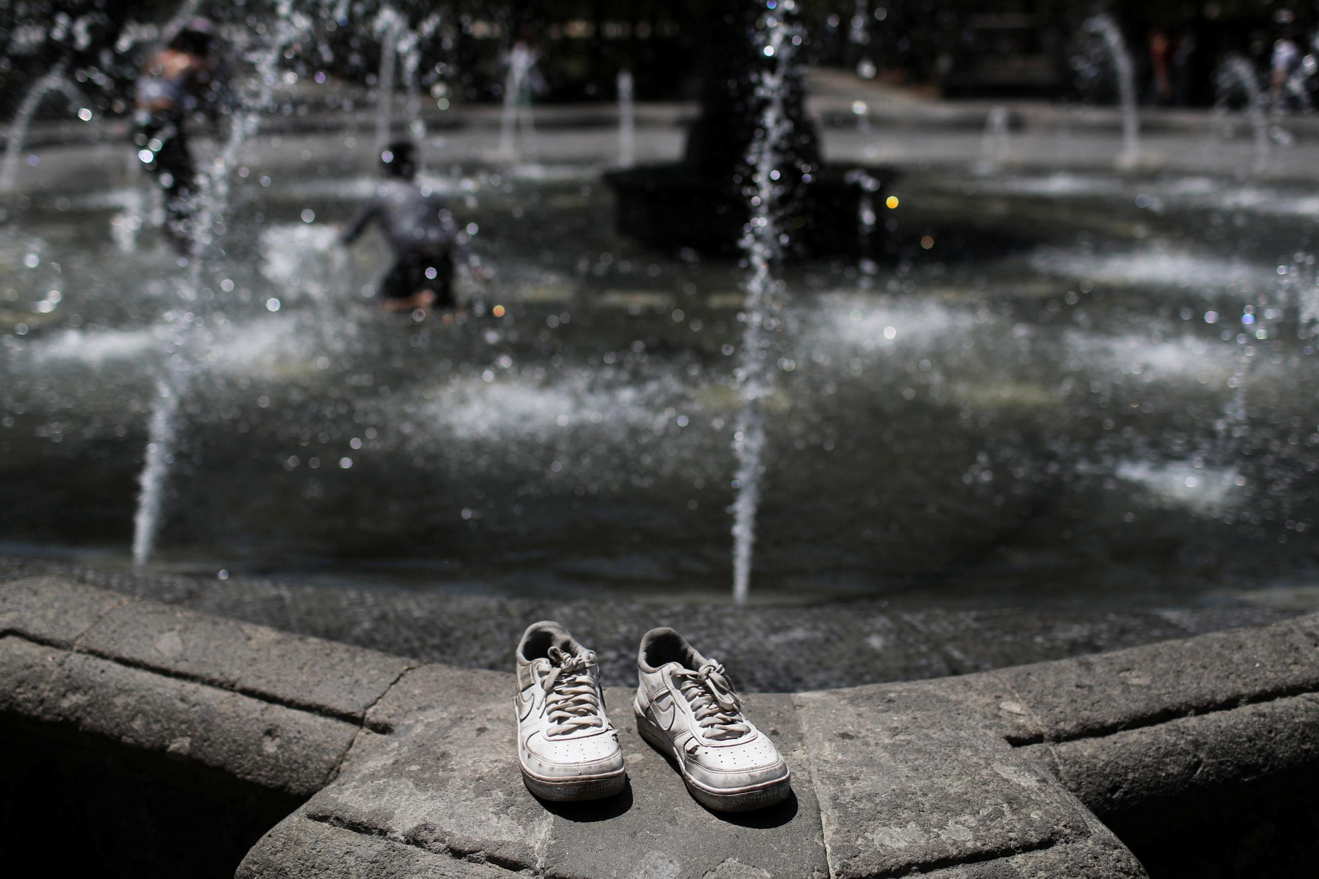The tennis shoes rest on a fountain during a heat wave.
