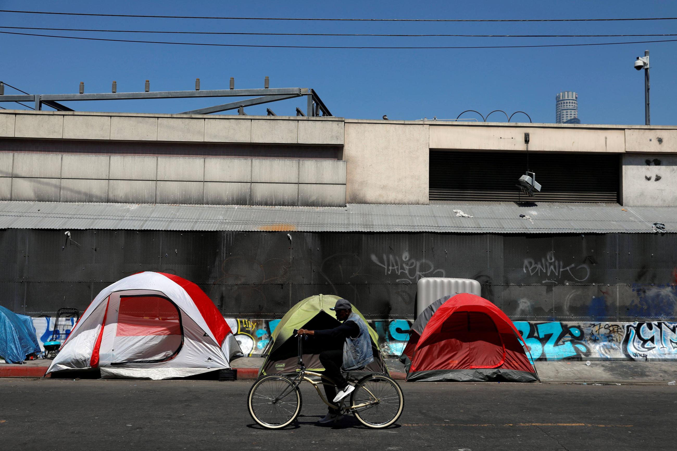 A cyclist passes by tents and tarps erected by homeless people along sidewalks in the skid row area of downtown Los Angeles, California, U.S., June 28, 2019