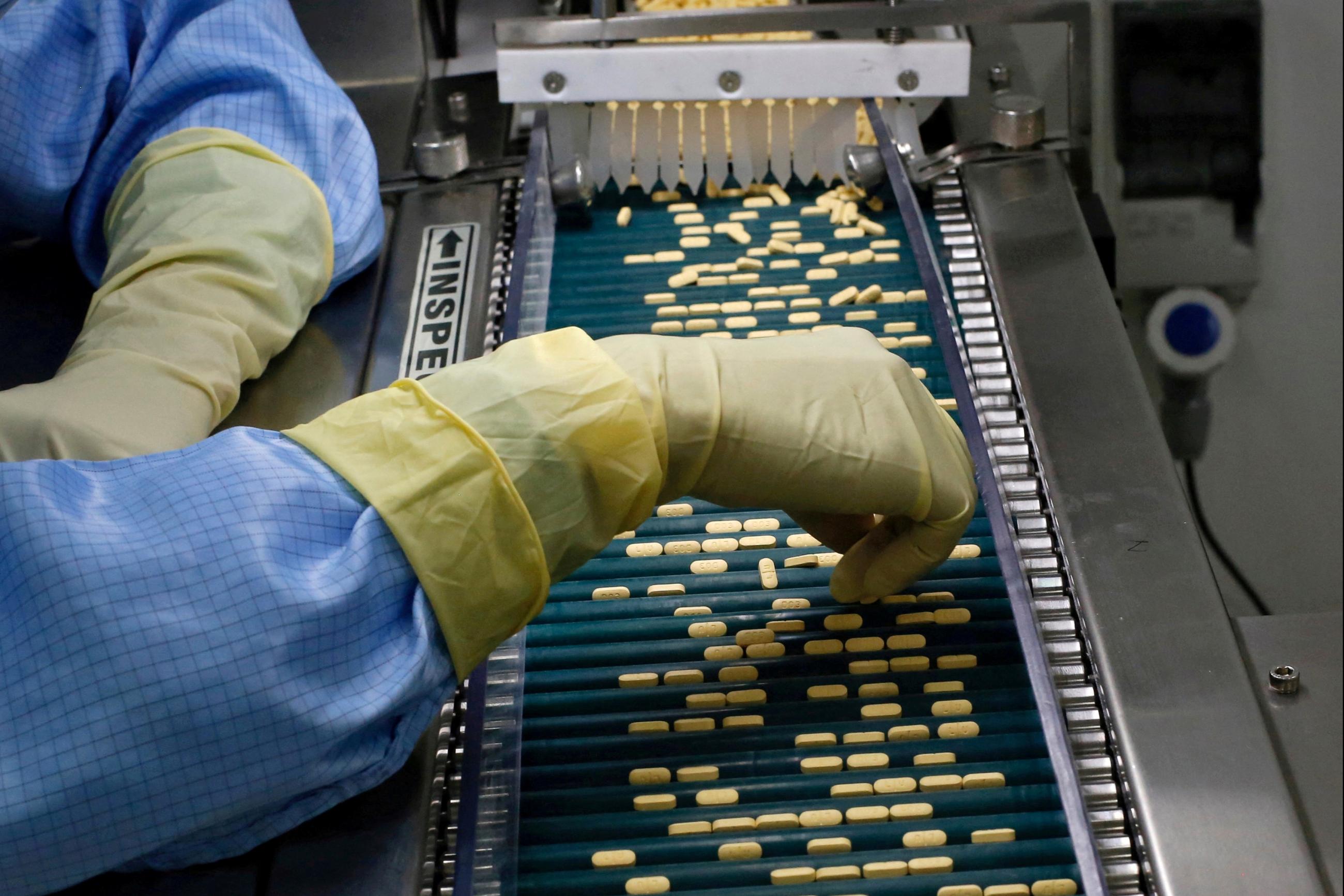 An employee inspects tablets as they move along the production line at a pharmaceutical plant of Lupin.