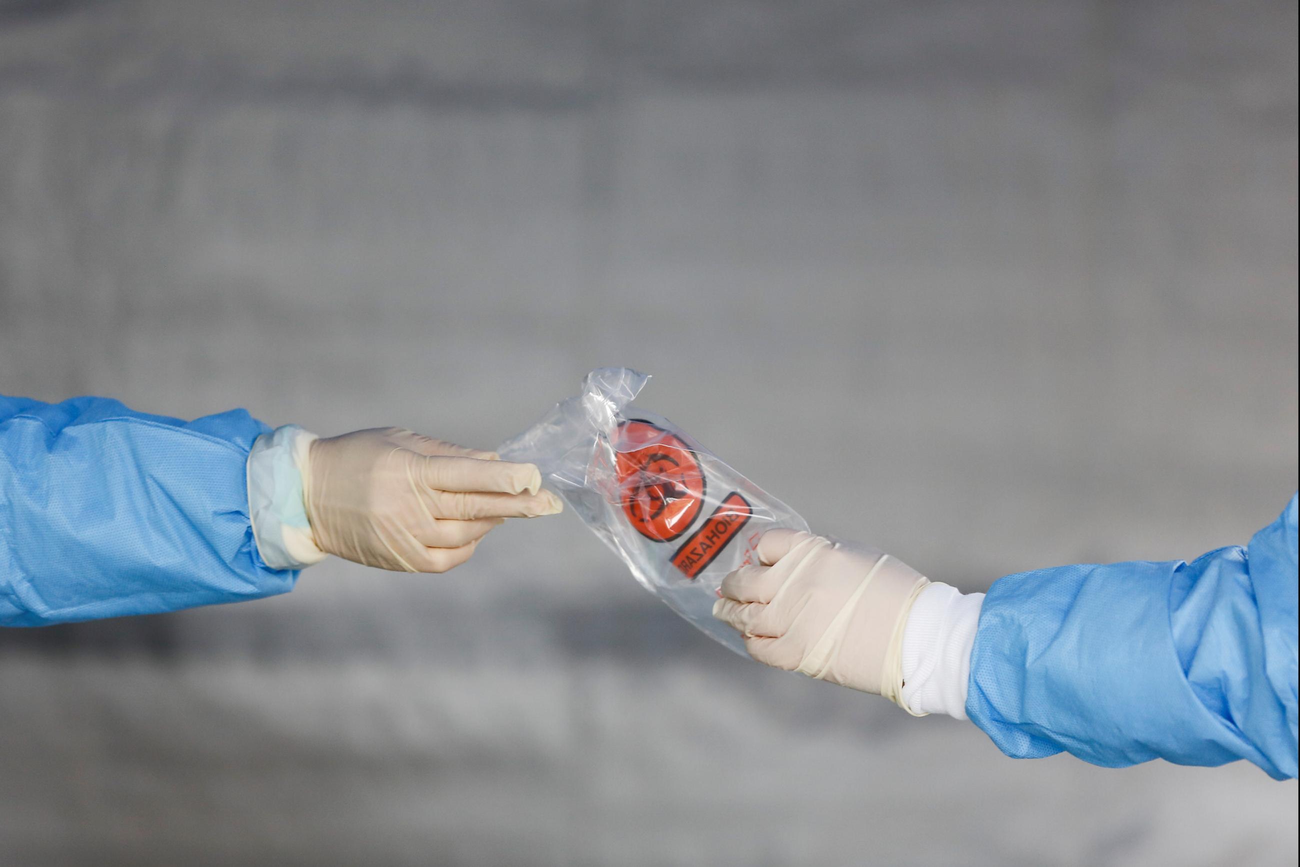 Health-care workers hand off a biohazard bag at a COVID-19 testing site outside the International Community Health Services, in Seattle, Washington, on March 26, 2020.