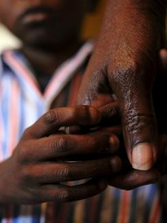 Nine-year-old Tumelo holds his grandmother's hand after taking his medication at Nkosi's Haven, south of Johannesburg, on November 28, 2014. Picture shows a large adult hand and the lower part of a child’s face in the background as his own hand grasps his grandmother’s. 