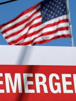 An entrance sign to the Texas Health Presbyterian Hospital in Dallas, Texas, on October 4, 2014. The sign says “EMERGENCY” and points to the left. In the background we can see an American flag billowing against a brilliant clear blue sky. 