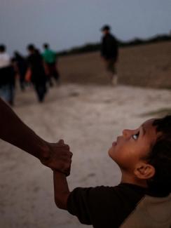 Picture shows Eduardo looking up pensively at his father at they walk along a road in what appears to be dusk or pre-dawn dim light. Luis is off-camera and only his arm visible. 