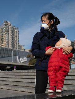 The baby has a puffy red jumpsuit, and she is wearing a black face mask. 