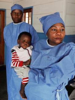 Photo shows Arlette holding the baby in front of a clinic while two other health workers stand in the background. 