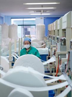 The photo shows a busy factory with a single worker standing amid spools of material on a busy assembly line. 