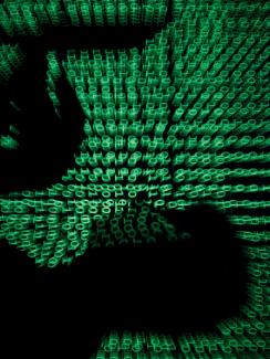 The image shows the silhouette of a man on a laptop with green ones and zeroes, reminiscent of the film "The Matrix" projected over the image. 