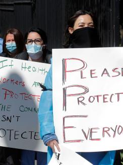 The photo shows a number of nurses lined up holding placards. One of them plays off the term PPE and spells out "Please Protect Everyone." 
