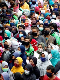 The photo shows a crush of people, many of them wearing face masks, crowded in all parts of the shot's frame. 