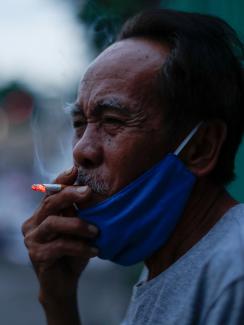 The photo shows a man with his mask pulled down taking a drag on his smoke. 