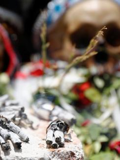 The photo shows two human skulls laid out with flowers in a ceremonial way with a number of burned cigarettes in the foreground. 