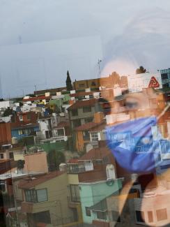 Picture shows the woman looking out her window and partially reflected in the glass. 