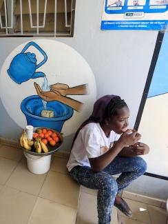 Picture shows a girl with a small basket of fruit sitting next to a large, blue UNICEF basin. 