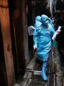 The photo shows workers in blue suits walking down a narrow alleyway. 