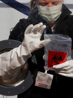 The photo shows the worker behind a protective barrier with incorporated gloves, allowing her to work with patients on the other side. 