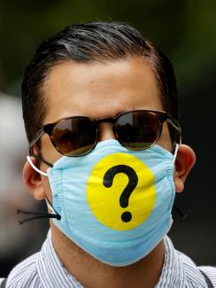 Picture shows a well groomed man who appears to be in his 30s wearing a mask adorned with a huge question mark. 