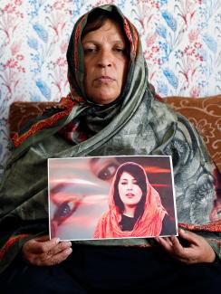 Picture shows the mother stermly looking at the camera holding a photo of her daughter. 