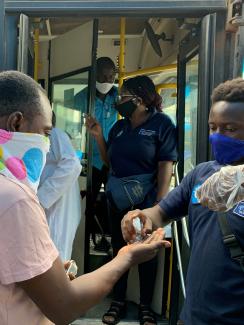  The photo shows a bus driver dispensing sanitizer to passengers as they board. 