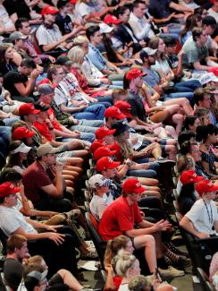 The photo shows a huge crowd of yound people, very few wearing masks, packed into theater-like seats. 