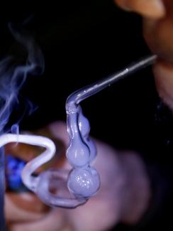 The photo is a closeup of a man smoking from a glass pipe. 