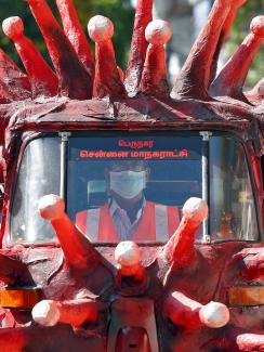 The image shows a vehicle painted red and covered with crown spikes reminiscent of the virus, which appear to be made of paper mache. 