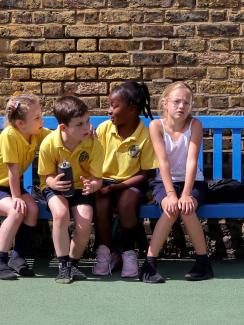 The photo shows four kids on a bench. One of them is looking at the camera. 