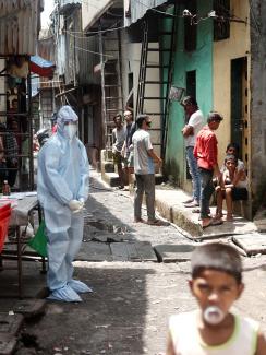 The photo shows a worker wearing personal protective equipment standing awkwardly among residents, most of whom aren't even wearing a mask. 