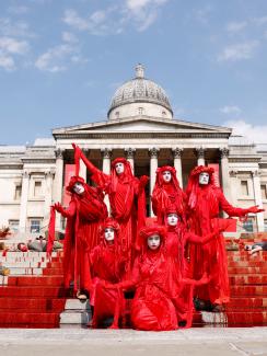 The photo shows a crowd of performance artists demonstrating with costumes and fake blood splashed everywhere. 