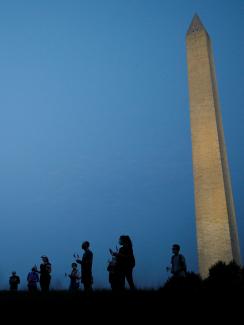 The photo shows the monument in the thin morning lite with a silhouette line of people standing in the foreground. 