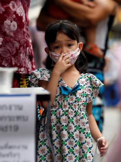 The photo shows a small girl wearing a facemask looking at the camera. 