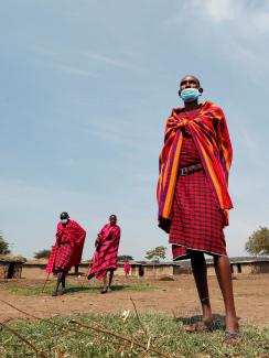 This is a striking photo that shows a number of the elders in brightly colored reddish clothing on a clear day against a backdrop of what appears to be a village. 