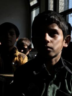 The photo shows a darkened classroom with several students facing the camera. 