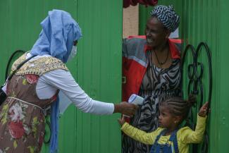 Woman health extension worker takes the temperature of a young girl outside a green door is Addis Ababa, Ethiopia. 