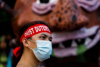 An activist wearing a statement band that writes "Oust Duterte" is photographed in front of an effigy dubbed "Duterte Virus" during a protest in Manila, Philippines on September 21, 2020.