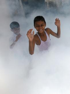 Children play as a health worker fumigates a residential area, where cases of malaria were reported, in Mumbai March 20, 2009. 