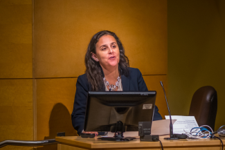 Dr. Patty García stands at a podium speaking. Dr. Garcia is professor and Dean of the School of Public Health at Universidad Peruana Cayetano Heredia in Lima, Peru. She is the former Minister of Health of Peru