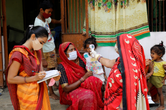 A health-care worker checks the temperature of a child as other adults and children watch during a door-to-door COVID-19 surveillance visit in a village on the outskirts of Ahmedabad, India on June 9, 2021.