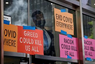A security person looks out from the entrance covered in signs saying end COVID to the Pfizer World Headquarters as activists rally for global access to the COVID-19 vaccine, in New York, July 14, 2021. 