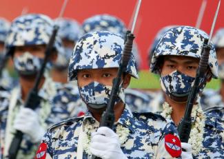 Soldiers in blue camouflage helmets and face masks stand in formation holding bayonets a parade on Armed Forces Day in Naypyidaw, Myanmar. 