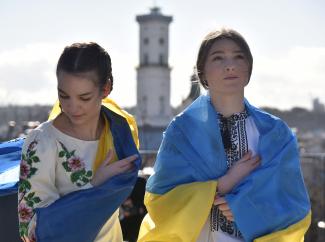 Two young women stand in Lviv, Ukraine, wearing traditional Ukrainian blouses and the blue and yellow flag of Ukraine