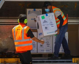 An air carrier worker in an orange vest transfers a box of Pfizer-BioNTech vaccine against the COVID-19 under the COVAX scheme at an airport in San Luis Talpa, El Salvador