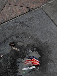 A protective face mask imprinted with the U.S. flag lays on the ground, amid the coronavirus disease (COVID-19) pandemic, as a person walks by outside Pennsylvania Station in New York City, U.S., October 5, 2021.