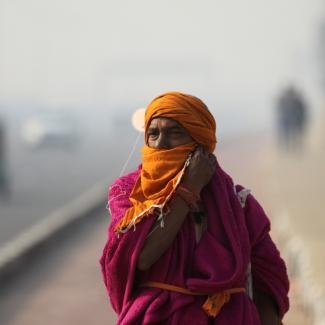 A Sadhu or a Hindu holy man robed in pink and orange adjusts a cloth on his face as he walks across a highway on a smoggy morning in New Delhi, India, November 18, 2021