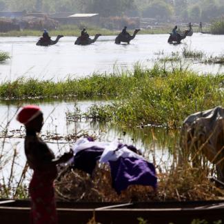 Men on camels cross the water as a woman washes clothes in Lake Chad in Ngouboua, Chad.