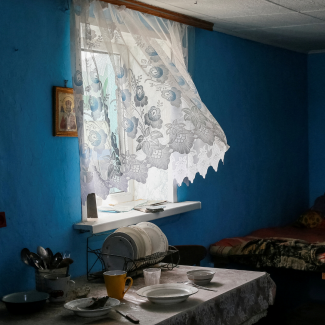 A white lace curtain flutters in the breeze in the window of a kitchen in a home in Kyiv, abandoned by residents during the Russian war on Ukraine, March 2022.