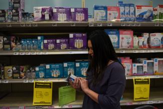 A mother with long brown hair reads the label of a formula can in front of partially empty grocery store shelves amid a nationwide shortage in Houston, Texas, on May 19, 2022. 