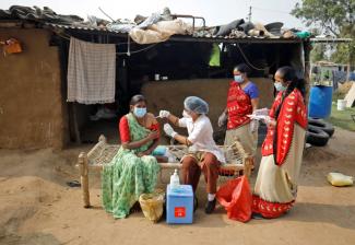 A woman in a green sari receives a dose of a COVID-19 vaccine manufactured by Serum Institute of India, outside her house during a door-to-door vaccination drive on the outskirts of Ahmedabad, India, on December 15, 2021. 